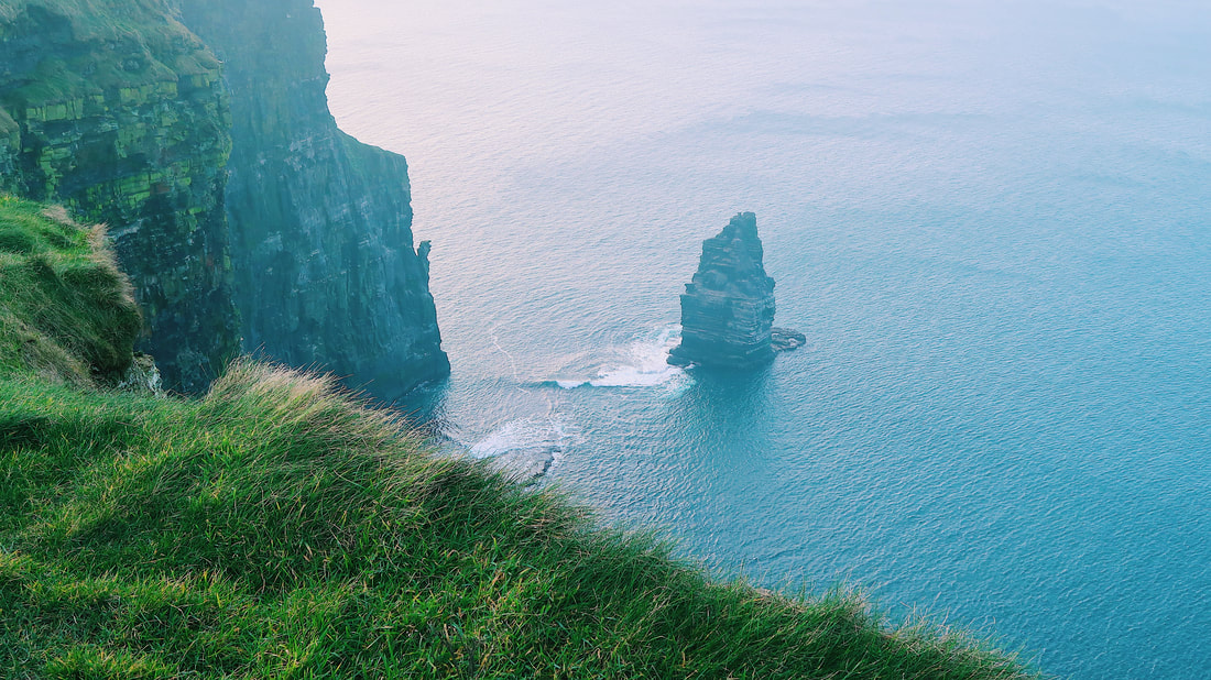 A photo of green grass and the cliffs of Ireland is shown. The water beside the cliffs is bright blue.