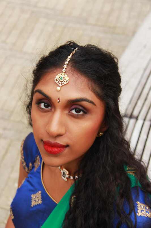 A woman stares up at the camera while wearing a bright red lip and a blue and green sari. 